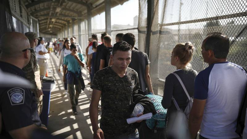 In this Aug. 2, 2019, file photo, migrants return to Mexico as other migrants line up on their...