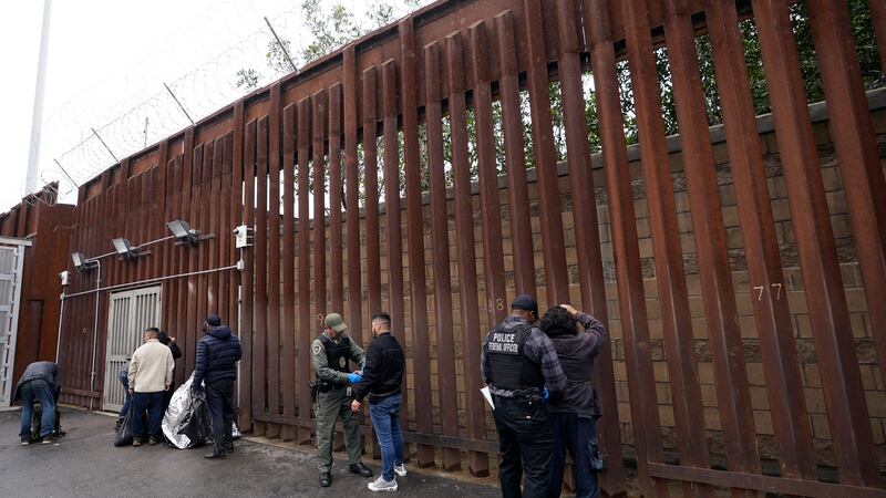 Federal officers remove handcuffs from men before releasing them through a gate in a border...