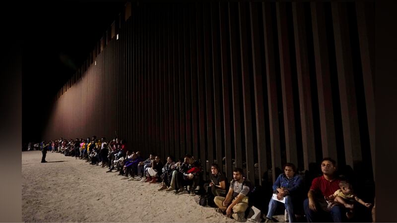 Migrants wait along a border wall on Aug. 23, 2022, after crossing from Mexico near Yuma, Ariz.