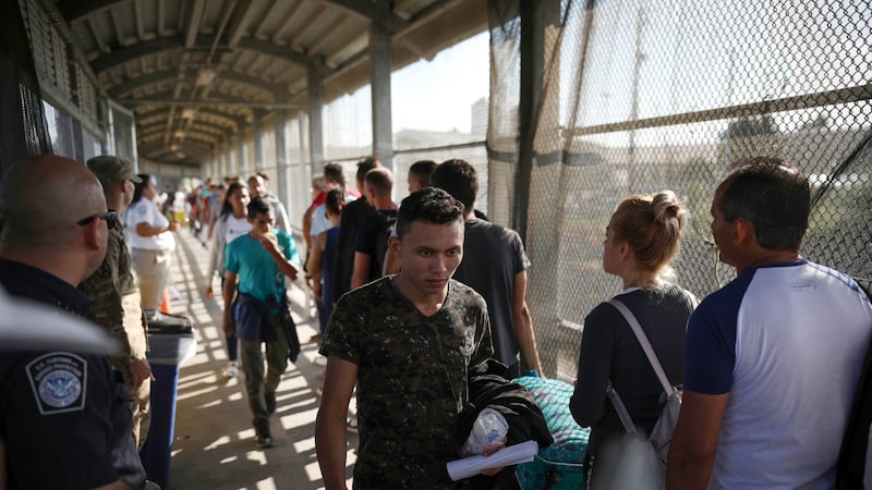 In this Aug. 2, 2019, file photo, migrants return to Mexico as other migrants line up on their...